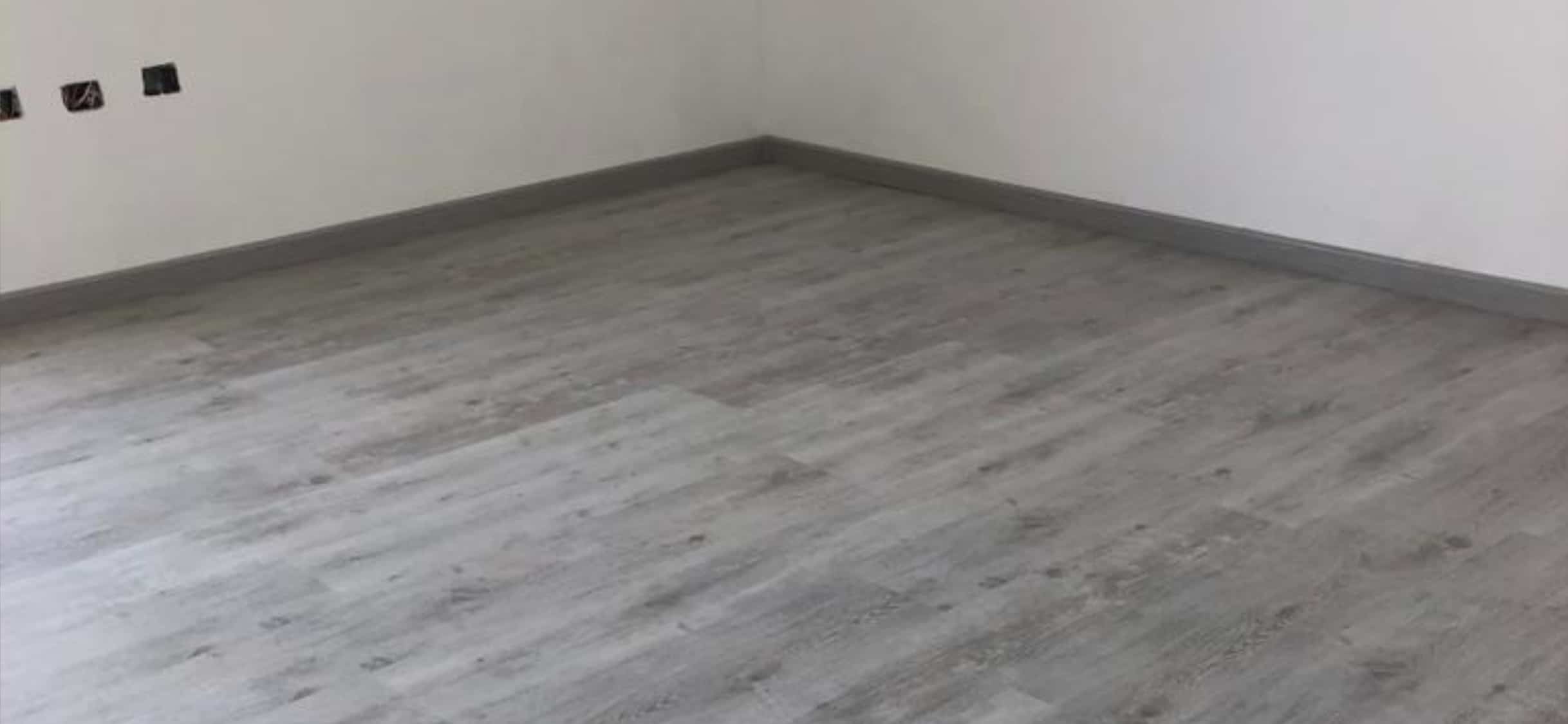 Esquina de una habitación en la que se puede observar un piso laminado gris 
